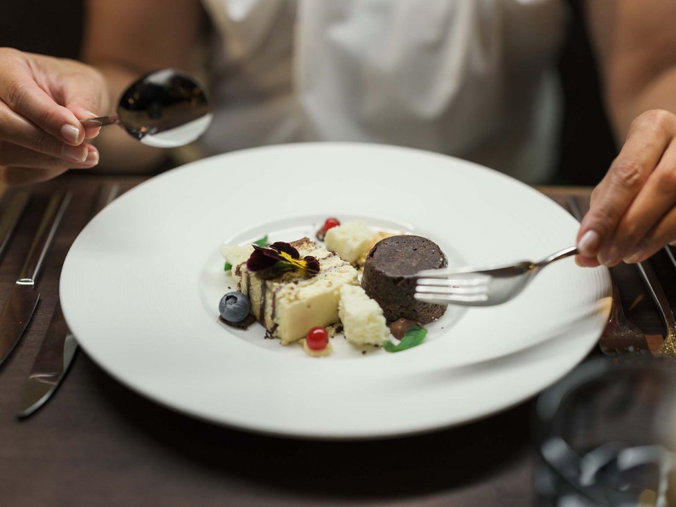 MOHR Genuss im Sporthotel in Österreich Person isst fein angerichtetes Dessert mit Gabel und Löffel