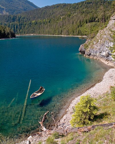 Ein Hotel mit Pool in Tirol – und zwei Badeseen Person rudert in einem Boot auf klarem Bergsee umgeben von Wald