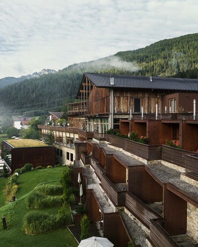Ein Blick zurück auf die Geschichte des MOHR life resort Holzhotel in einem grünen Bergtal mit Nebel und bewaldeten Hügeln