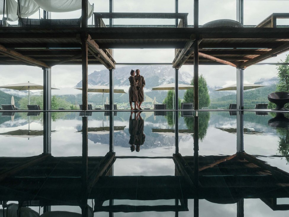 Großzügig und exklusiv: Ihr Wellnessurlaub in Tirol Paar in Bademänteln neben einem Innenpool mit Bergblick