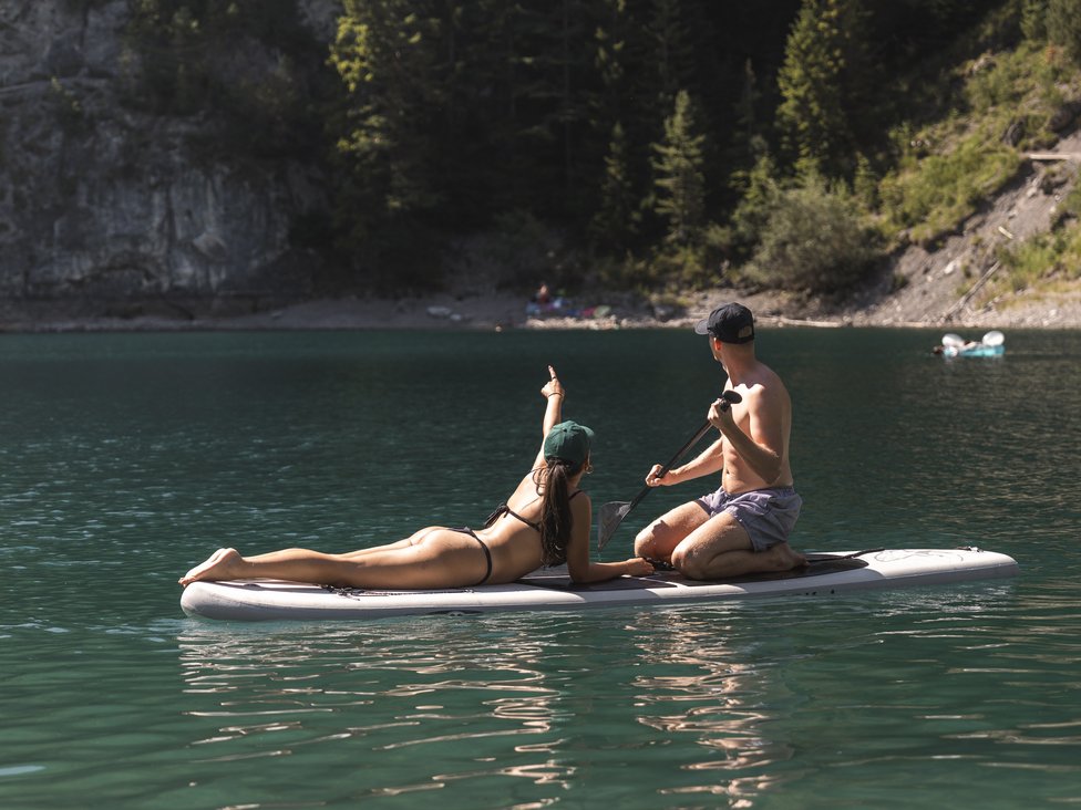 Wellness und Luxus: Ihr Hotel in Tirol Paar auf einem Paddleboard auf ruhigem Bergsee umgeben von Tannen