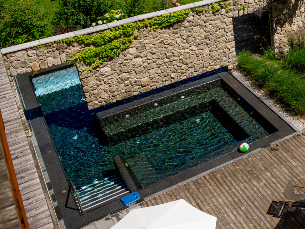 Großzügig und exklusiv: Ihr Wellnessurlaub in Tirol Modernes Schwimmbecken mit Steinstützmauer und Balkon