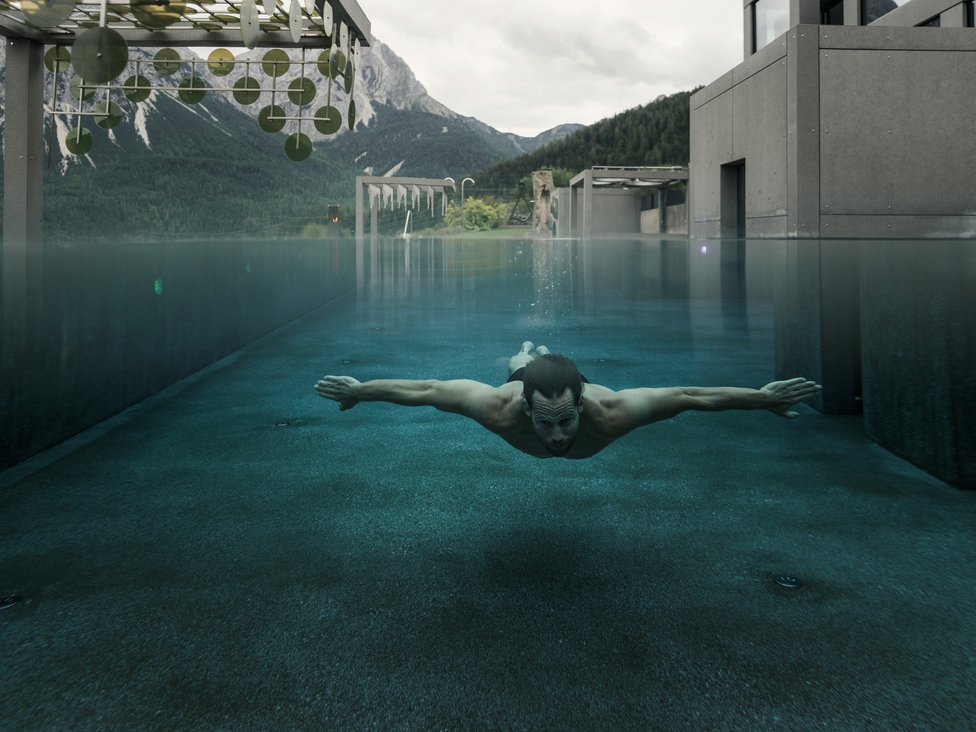 Großzügig und exklusiv: Ihr Wellnessurlaub in Tirol Mann schwimmt unter Wasser in modernem Pool mit Bergblick