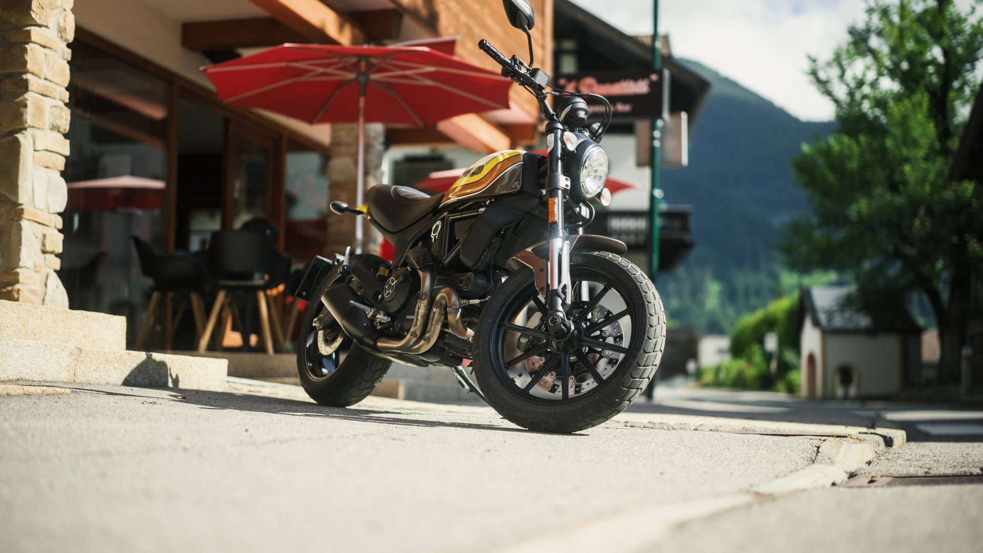 MOHR Sport bedeutet MOHR fun. Schwarzes und gelbes Motorrad auf Gehweg vor Café mit rotem Sonnenschirm