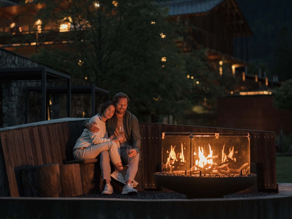Wellness und Luxus: Ihr Hotel in Tirol Paar sitzt abends entspannt am Feuer vor einem beleuchteten Gebäude in den Bergen