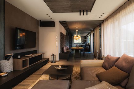 MOHR life resort News Modernes Wohnzimmer mit brauner Couch, TV und Essbereich im Hintergrund