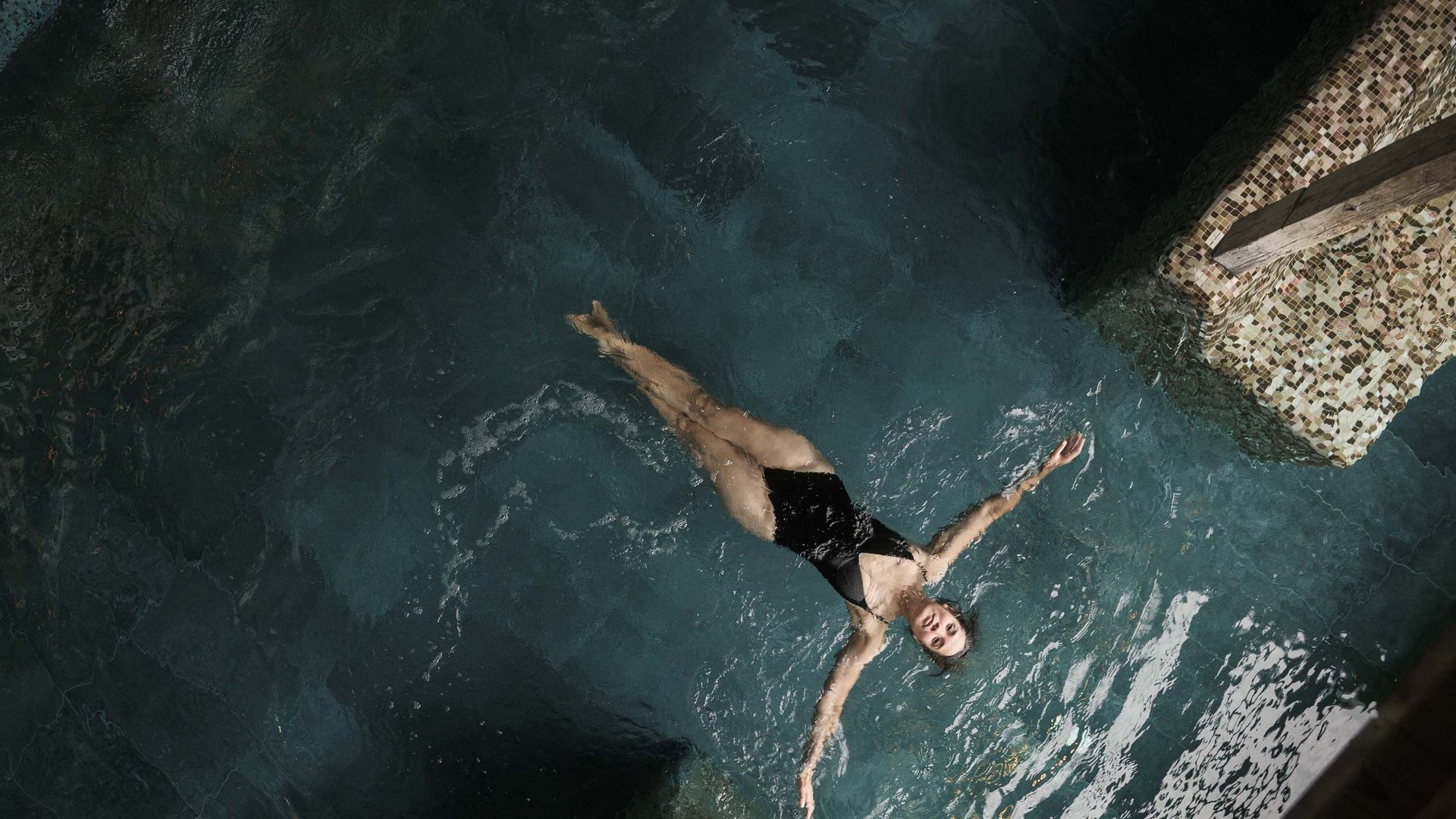 MOHR life resort Bildergalerie Frau im schwarzen Badeanzug liegt entspannt auf dem Wasser in einem Pool