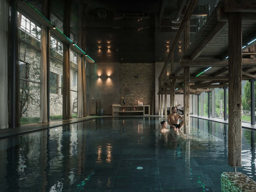 Großzügig und exklusiv: Ihr Wellnessurlaub in Tirol Innenblick auf einen Pool mit zwei Personen und Holzbalken im modernen Spa