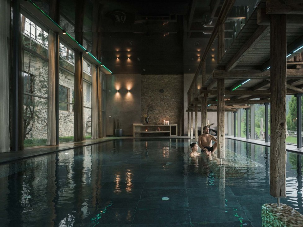 Großzügig und exklusiv: Ihr Wellnessurlaub in Tirol Innenblick auf einen Pool mit zwei Personen und Holzbalken im modernen Spa