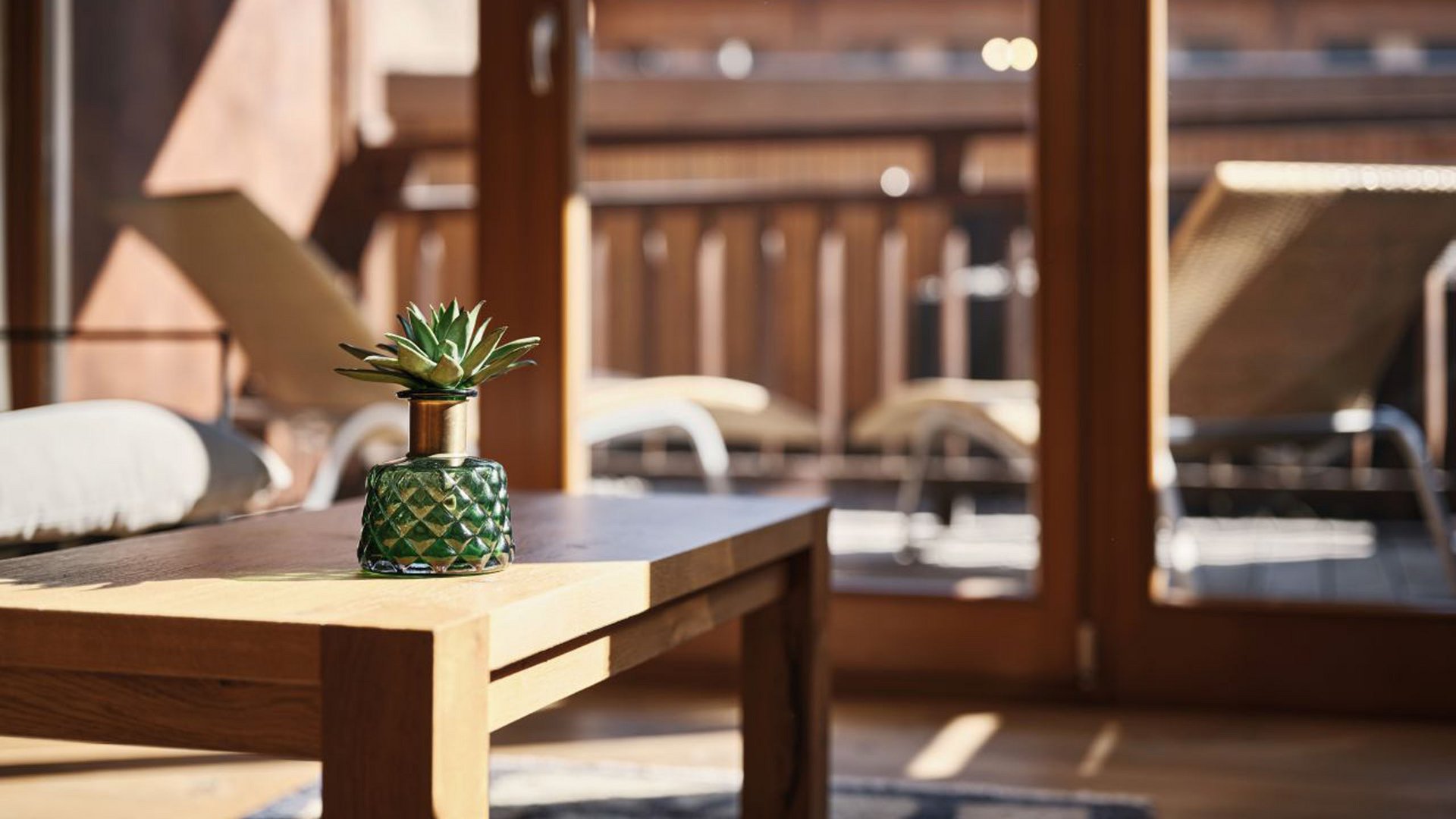MOHR life resort Bildergalerie Grüne Pflanze in Glasvase auf Holztisch vor Balkon mit Liegestühlen