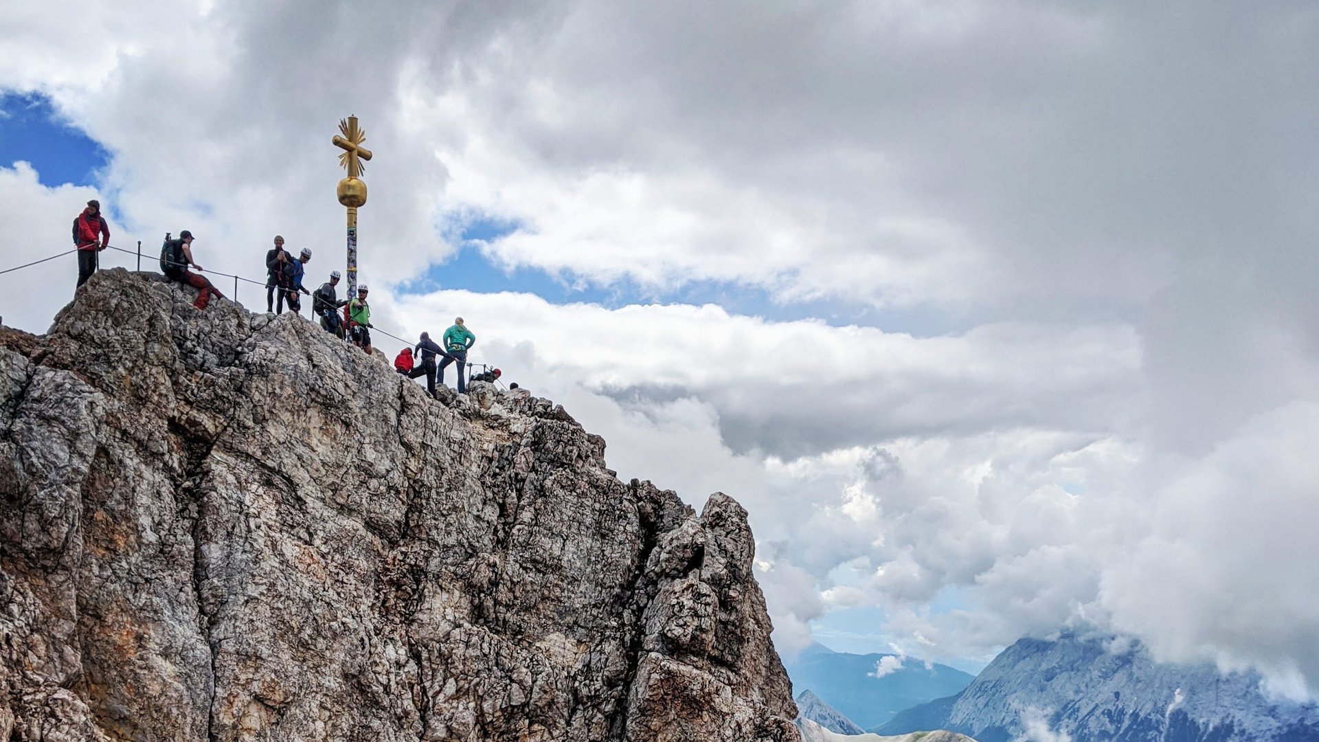 DAS Wellnesshotel am Fuß der Zugspitze Österreich Berggipfel mit Wanderern und Gipfelkreuz unter bewölktem Himmel