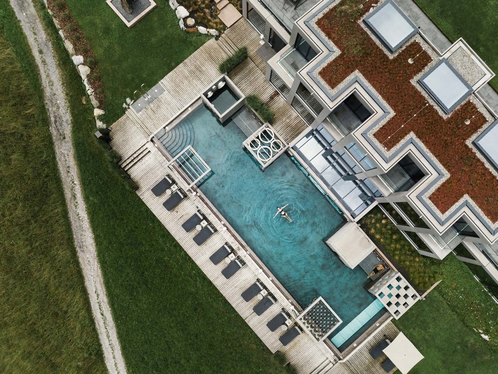 Großzügig und exklusiv: Ihr Wellnessurlaub in Tirol Luftaufnahme eines Pools mit Person und Liegestühlen neben modernem Gebäude