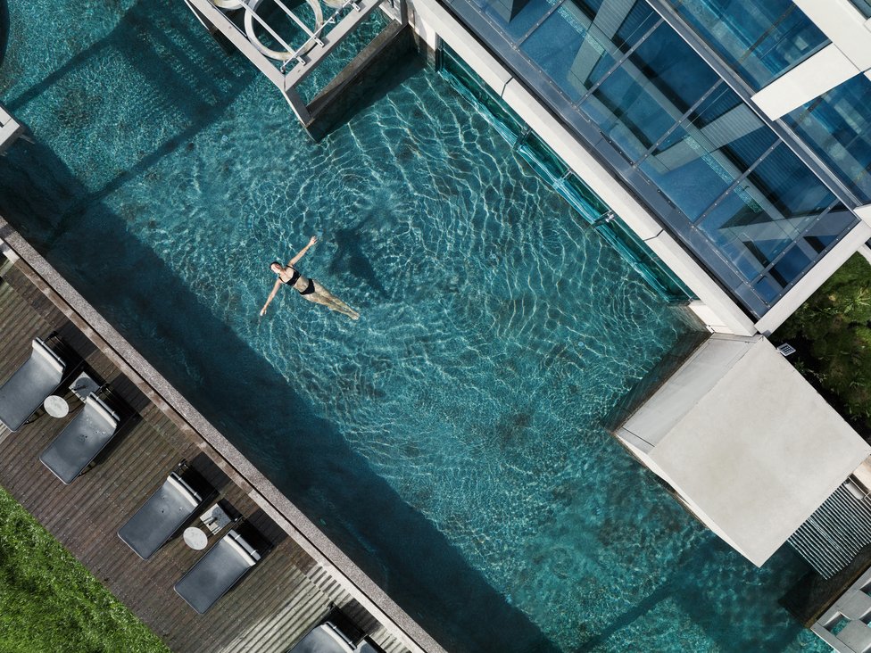 Wellness und Luxus: Ihr Hotel in Tirol Frau schwimmt entspannt in einem modernen Außenpool neben einem Gebäude