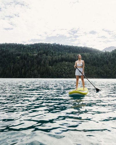 MOHR Sport bedeutet MOHR fun. Frau steht auf Paddleboard auf See vor bewaldeten Bergen