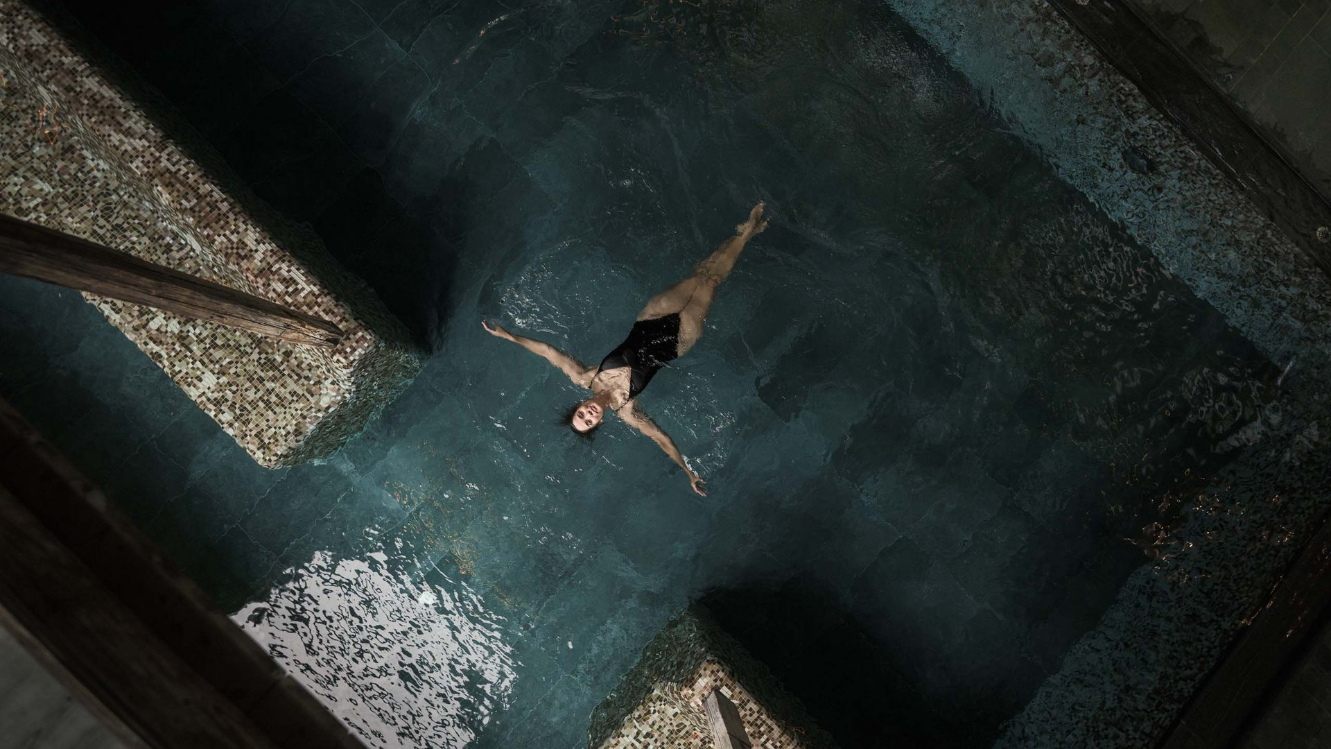Wellness und Luxus: Ihr Hotel in Tirol Frau entspannt und treibt auf dem Rücken in einem dunklen Schwimmbad