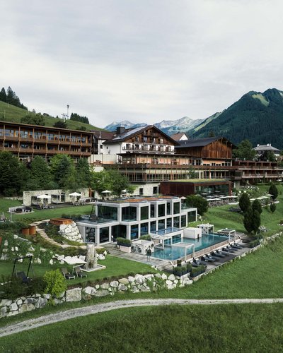 Ein Blick zurück auf die Geschichte des MOHR life resort Hotelanlage mit Außenpool und Liegen in den Bergen bei bewölktem Himmel
