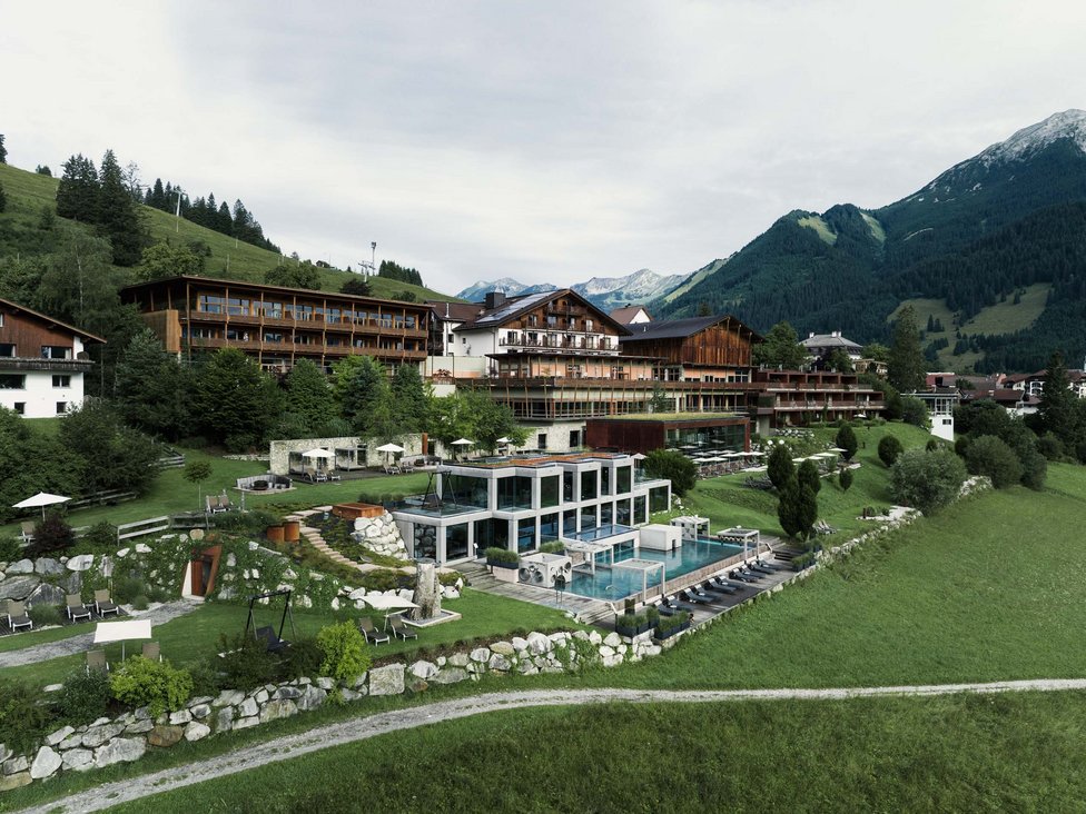 Großzügig und exklusiv: Ihr Wellnessurlaub in Tirol Hotelanlage mit Außenpool und Liegen in den Bergen bei bewölktem Himmel