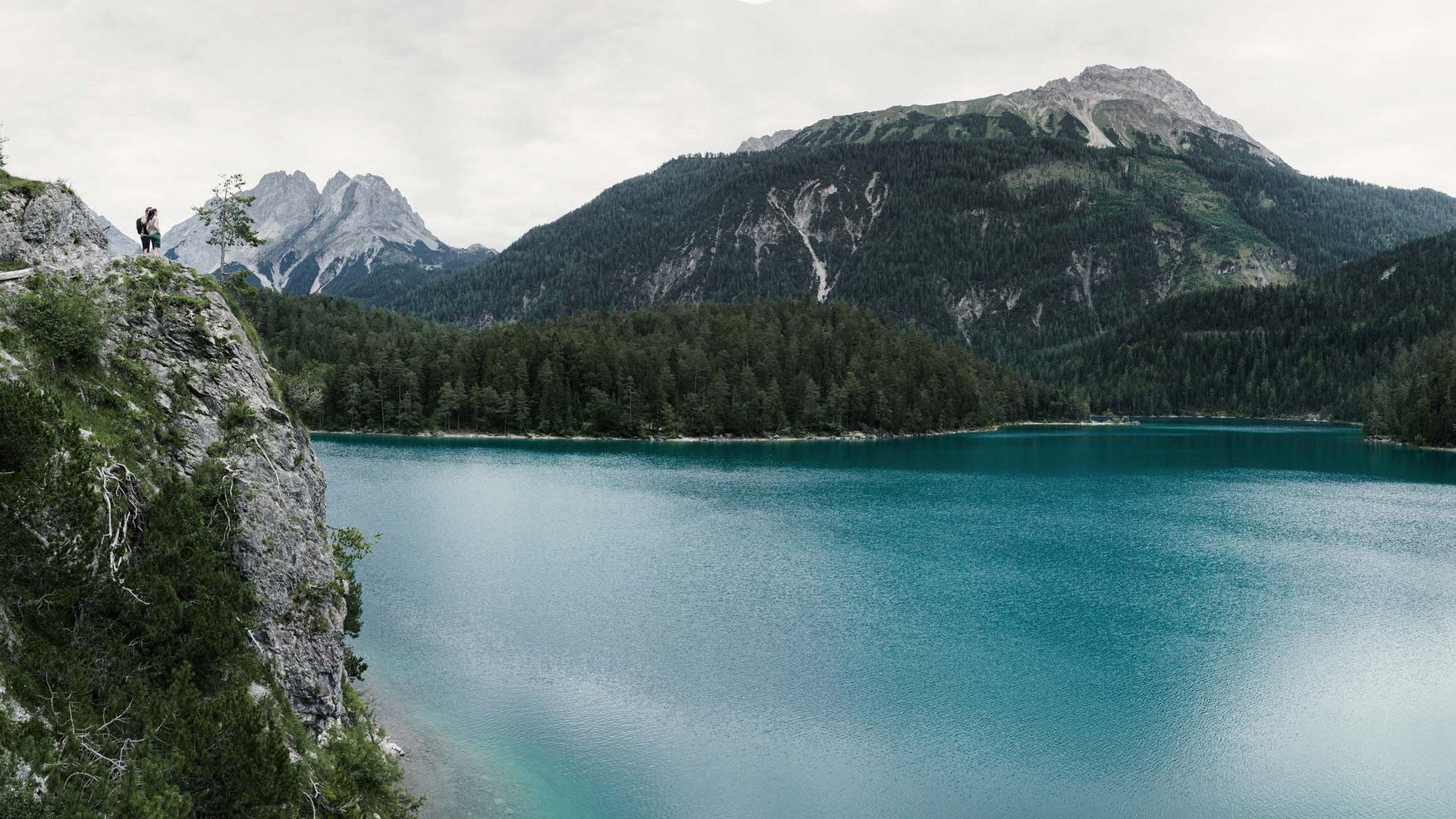 Wasservielfalt rund um Ihr Wellnesshotel in Tirol Zwei Wanderer stehen auf einer Klippe über einem blauen Bergsee