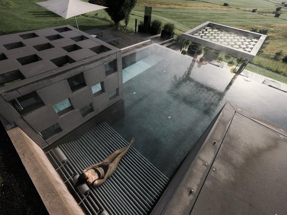 Großzügig und exklusiv: Ihr Wellnessurlaub in Tirol Frau entspannt in modernem Pool mit Sitzplatz und ländlicher Aussicht